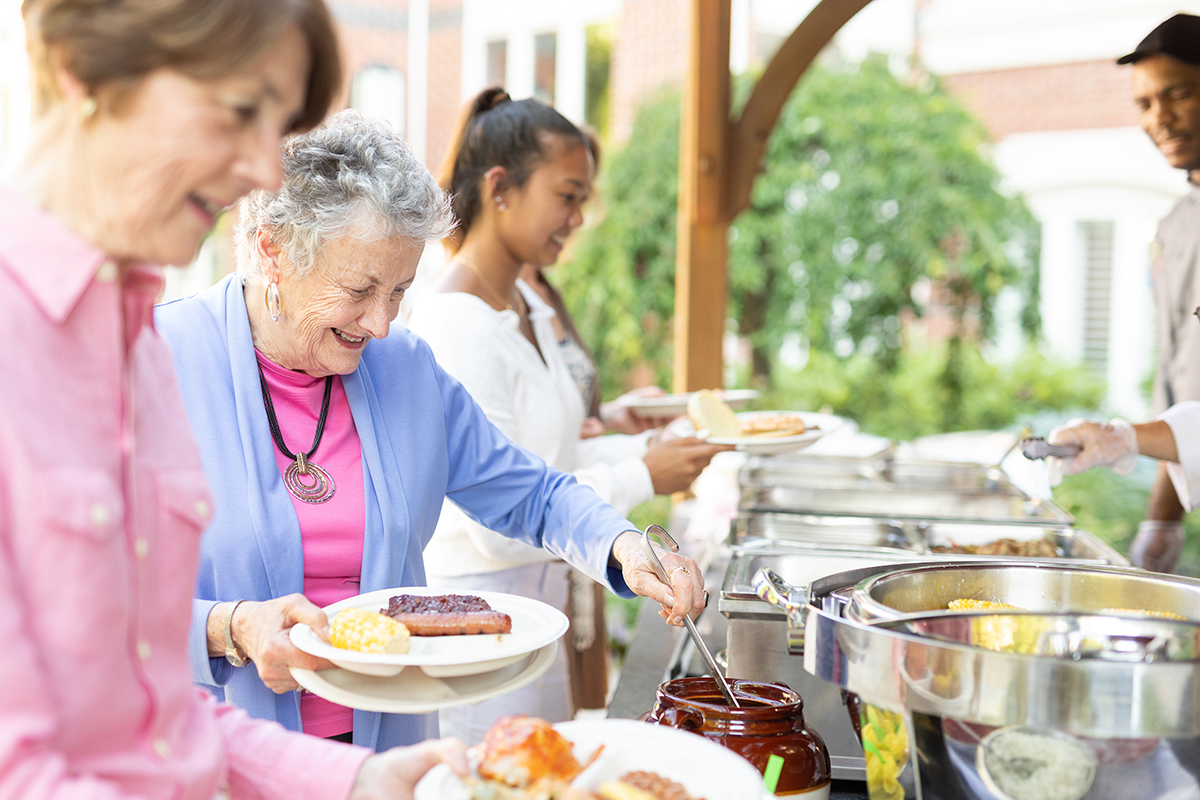 People in a buffet line outdoors getting food.